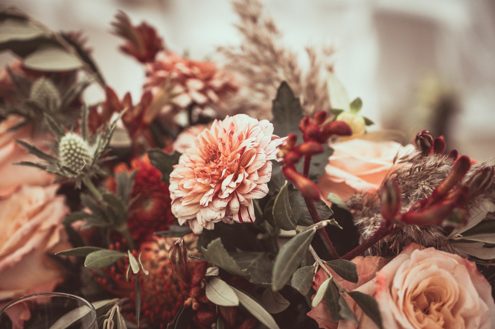 An autumn arrangement of peach and rust blooms with soft foliage, gathered in a glass vase.
