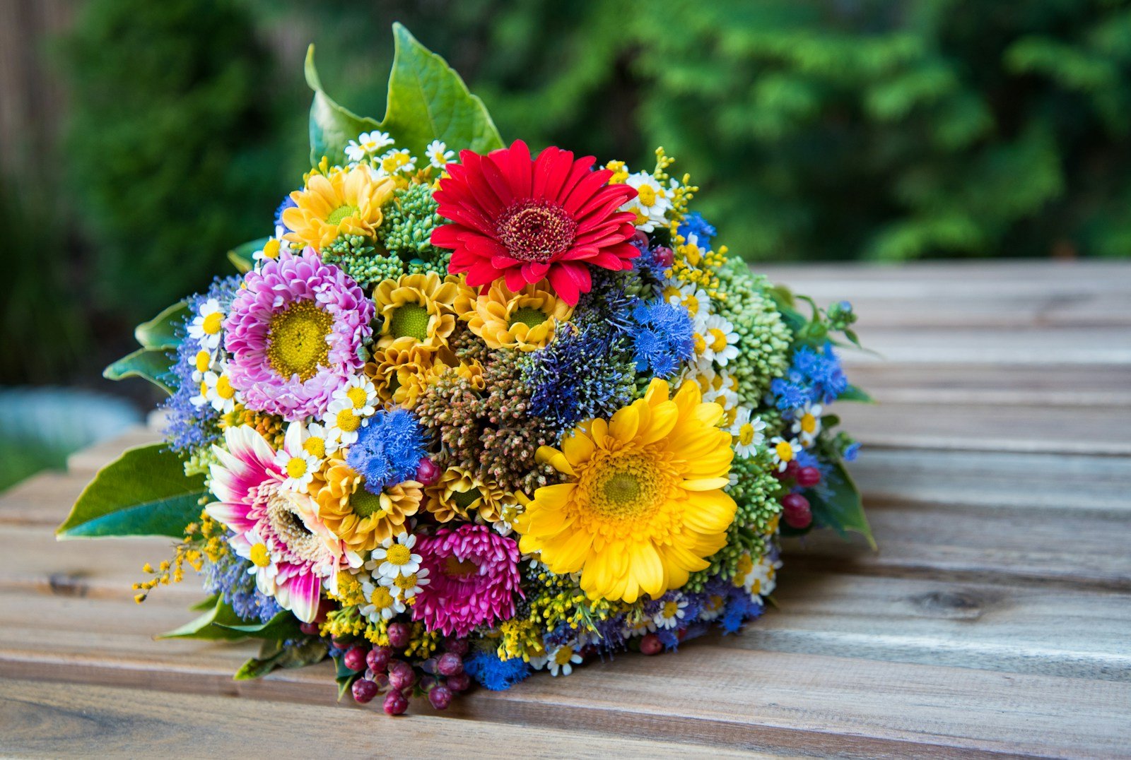 A vibrant bouquet of red, yellow, pink, and blue flowers rests on a wooden surface.