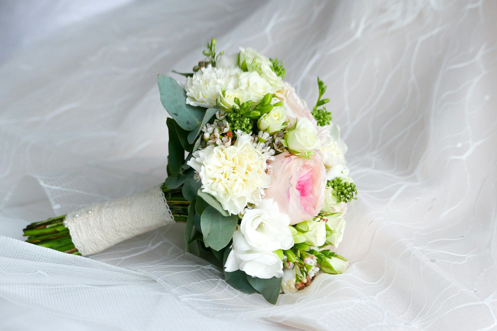 A bouquet of white and pink flowers with green leaves rests on a white textured fabric.